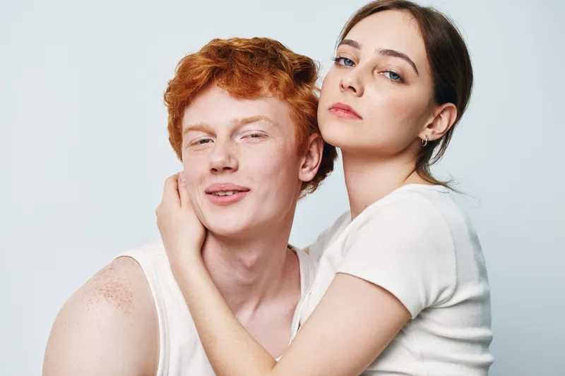 Young couple with woman embracing redhead man posing together on white background. Portrait of affectionate loving people showing close relationship and connection.