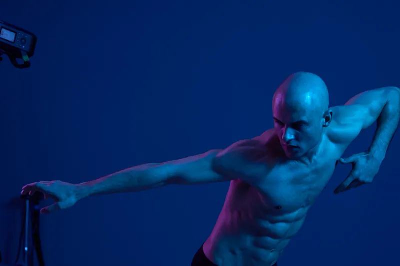 Athletic man posing dramatically in a vibrant light, showcasing strength and motion. The image features a captivating blend of blue and purple tones.