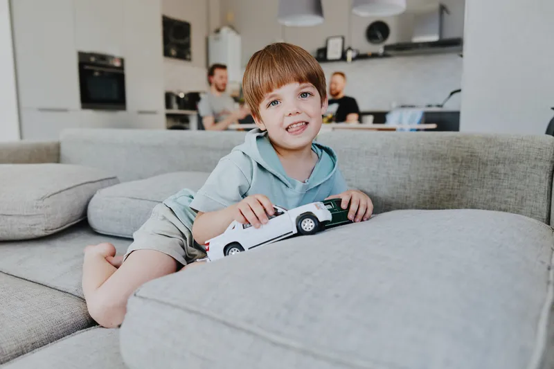 Happy boy playing with a toy car in a cozy modern living room. Bright colors and casual style create a joyful atmosphere for fun and creativity.