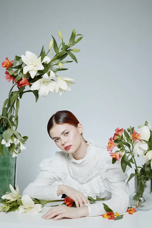Young woman with flowers wearing a white blouse, showcasing elegance and tranquility in a soft pastel setting, ideal for wellness and fashion concepts