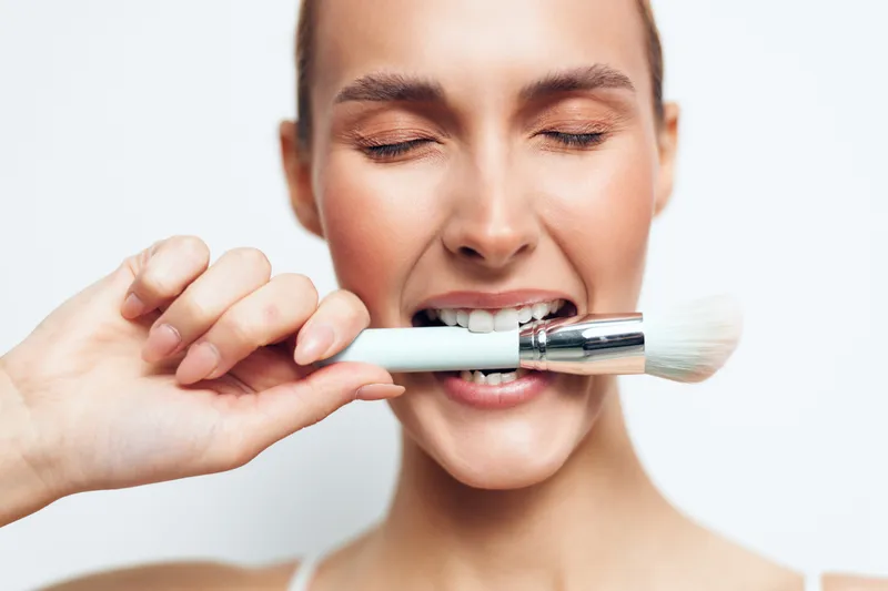 Smiling woman applying makeup with a brush, close up on white background, soft studio lighting, clean fresh complexion, beauty care and skincare routine, self care wellness mood calm