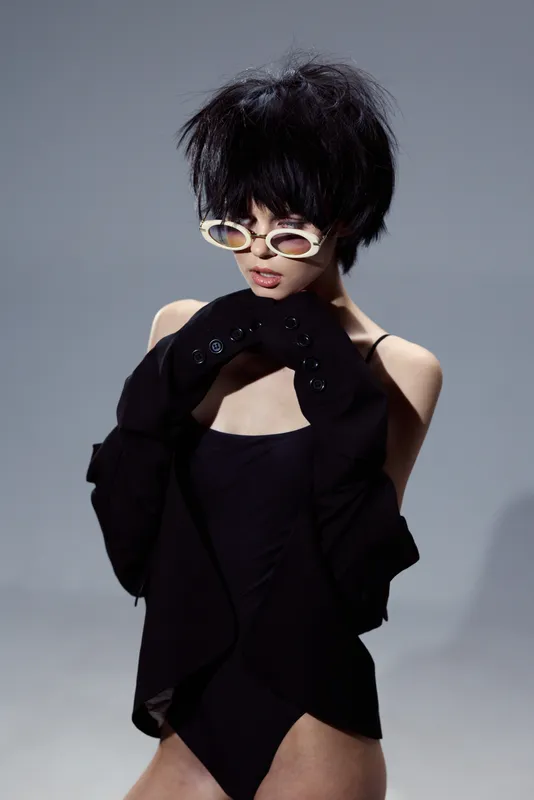 Stylish woman with short hair wearing sunglasses and black clothing posing in studio lighting