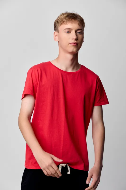 Man in a red t shirt stands in a studio, casual pose with a clean backdrop, soft lighting, and neutral mood suitable for lifestyle and fashion stock use