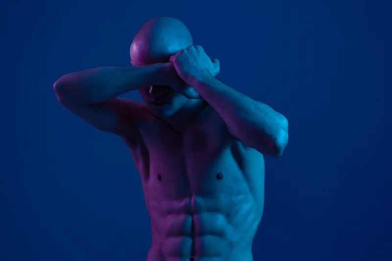 Man covering his eyes with hands, expressing vulnerability and introspection. The image captures a dynamic interplay of blue light and shadows, enhancing emotional depth.