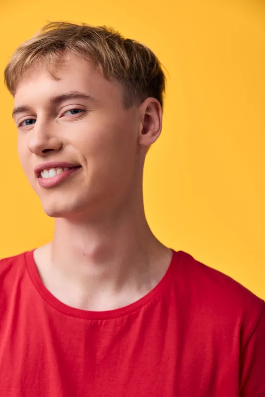 Young man smiling in a red shirt against a bright yellow background, casual studio shot showing confidence and style, ideal for fashion, lifestyle, and model portfolio use
