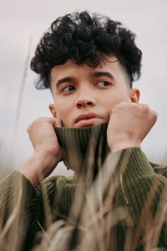 A candid portrait of a young person outdoors in a chunky knit sweater, conveying authenticity through natural lighting, subtle expression, and honest mood.