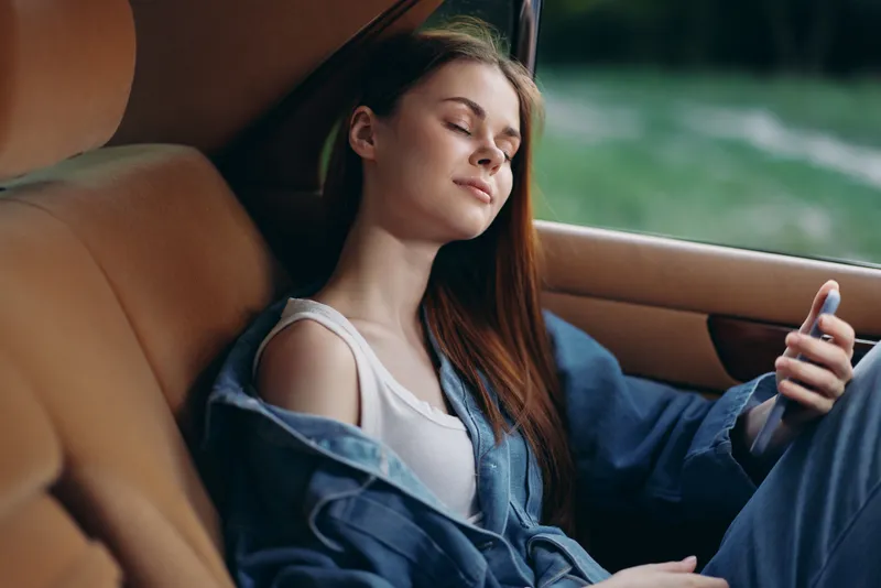 A serene young woman with long brown hair relaxes in a car, showcasing a comfortable denim outfit, evoking feelings of calm and tranquility in nature.