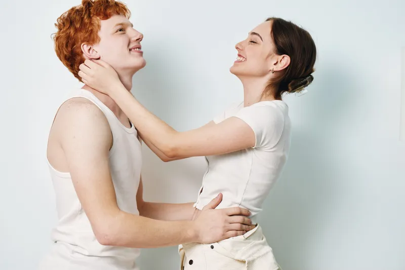 Young couple smiling and hugging in casual clothes on white background. Man and woman facing each other enjoying moment with happy expressions and close connection.