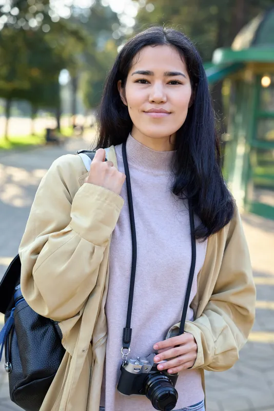 Woman with camera in a park, casual jacket and bag ready for outdoor photography, exploring nature and park scenes with relaxed style and candid vibe