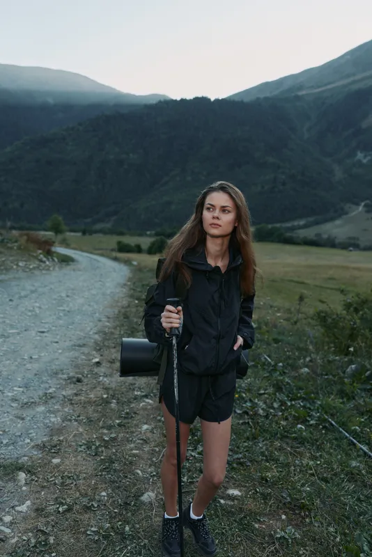 A young outdoor enthusiast stands on a rocky path in a mountainous valley with camera gear, ready to shoot, exuding focus and adventure under expansive skies.