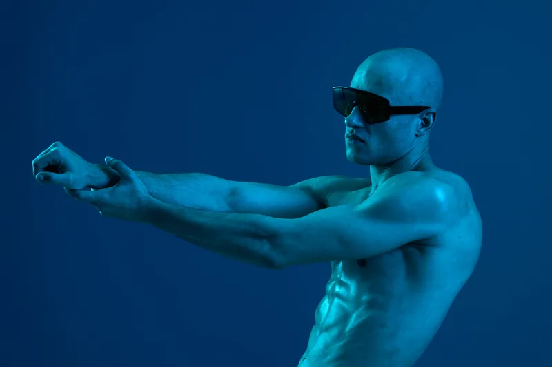 Strong man stretching in blue light, showcasing fitness and determination. The image captures a dynamic pose emphasizing strength and focus, creating an athletic vibe.