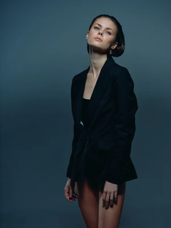 Elegant woman wearing black blazer with confident expression on dark background in studio setting