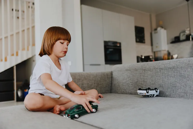 A young boy playing with toy cars on a cozy couch in a modern living room, showcasing creativity and imagination during playtime. The vibrant colors enhance the lively atmosphere.