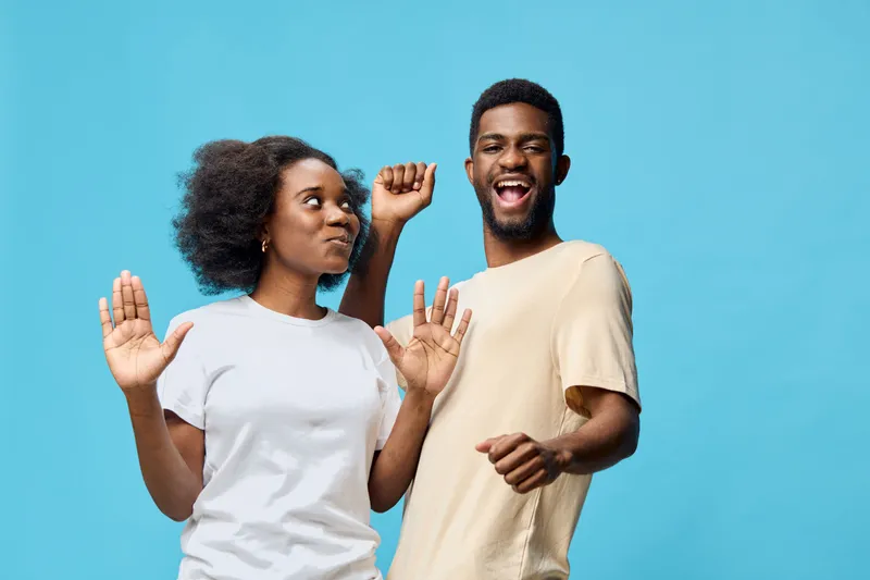 Happy African American couple dancing joyfully against a bright blue background, showcasing carefree emotions and casual attire perfect for fun moments
