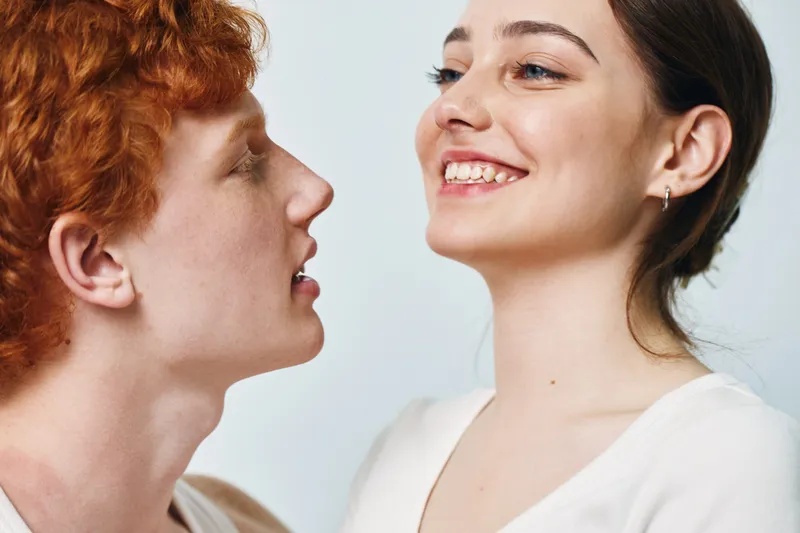 Young couple smiling and looking at each other with joy and affection in closeup portrait. Man and woman with positive emotions on light background in casual clothes.