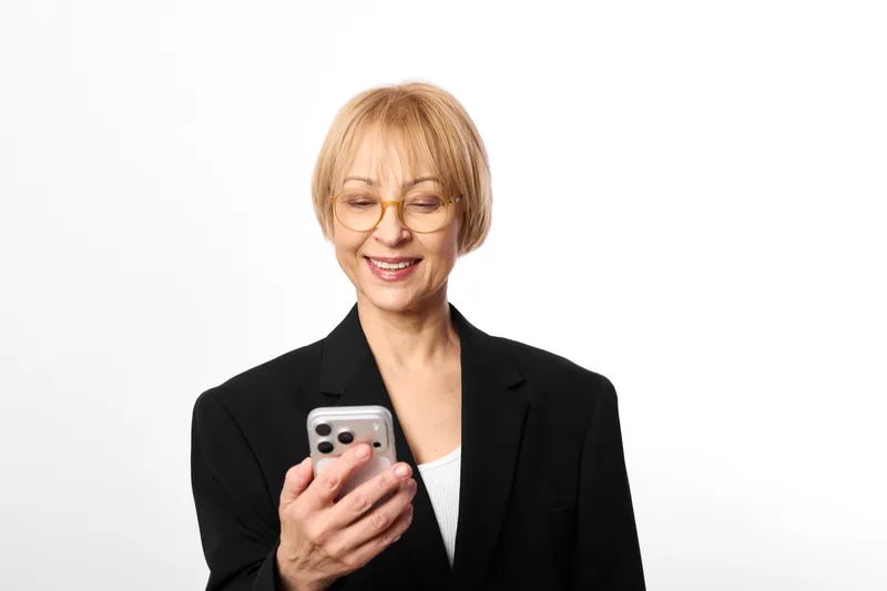 Woman with smartphone, communication for business, portrait of smiling mature woman, short hair, black blazer, white studio background, looking at screen, concept of digital connection and confidence