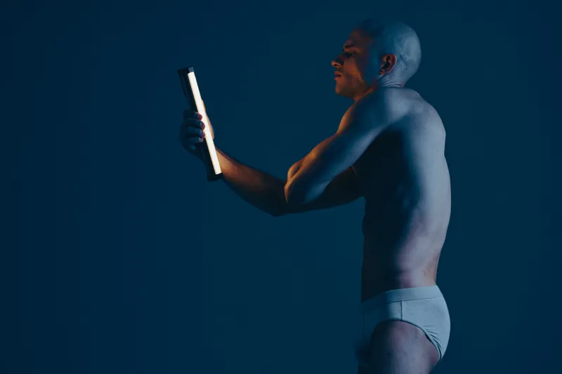 Confident man holding a light device, showcasing an artistic black and white composition. The focus highlights the interplay of shadows and light, enhancing the mood.