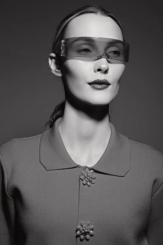 Portrait of a pale skinned Caucasian woman wearing futuristic translucent glasses and a textured buttoned shirt in a monochrome studio. Concept of fashion and modern style.