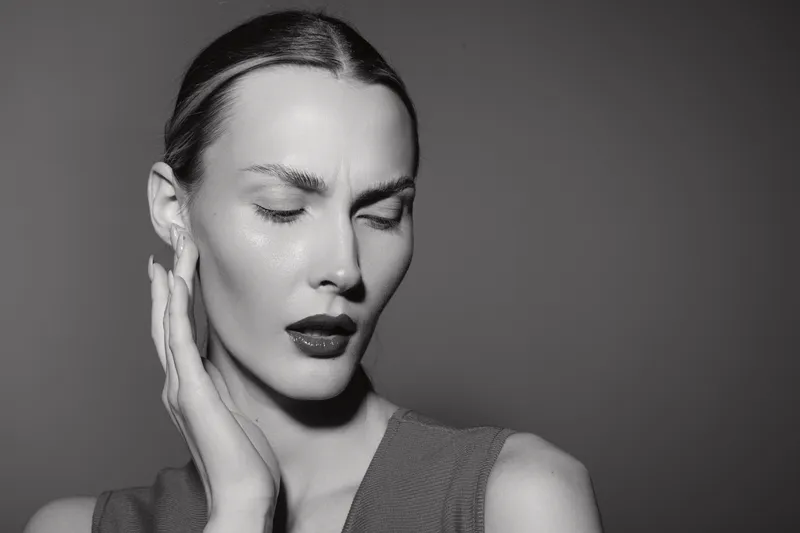 Portrait of a serious white woman with light skin and slicked back hair touching her face with closed eyes in monochrome. Concept for beauty, emotion, and minimalism.