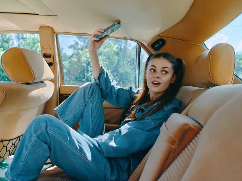 Young woman in denim outfit enjoying a carefree moment in a vintage car, smiling and playful, capturing the essence of freedom and nostalgia.