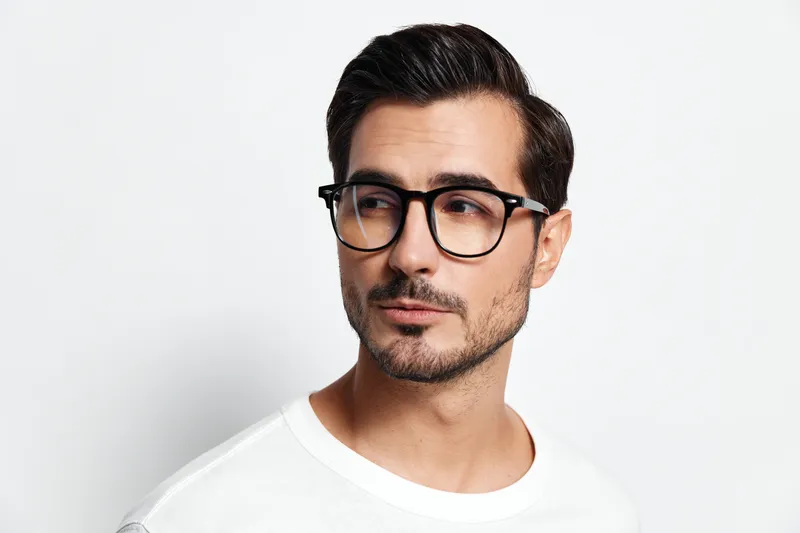 Handsome young man with glasses looking thoughtfully to the side, wearing a casual white t-shirt, against a simple light background. Stylish portrait concept.