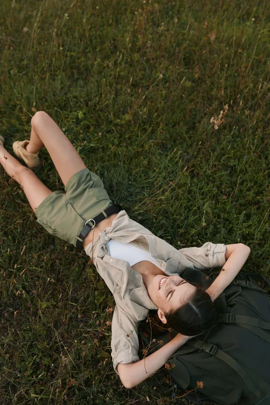 Relaxed woman lying on grass in casual attire, outdoor lifestyle scene, natural light, calm mood, carefree moment, nature setting, warm sunlight, peaceful repose, soft breeze, candid feel.
