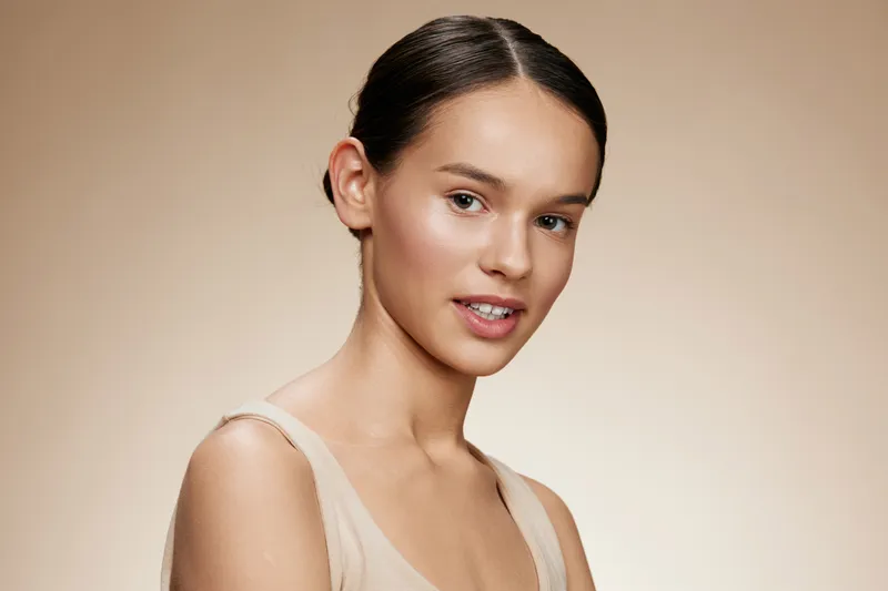 A young woman with an elegant demeanor, wearing a neutral toned outfit, exuding confidence against a soft beige background, perfect for beauty and skincare themes