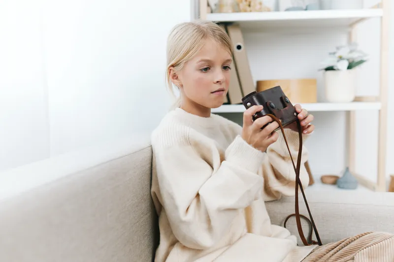 Authentic lifestyle image featuring a young student at home, focused on a camera, capturing a candid moment that blends play, study, and daily school life.