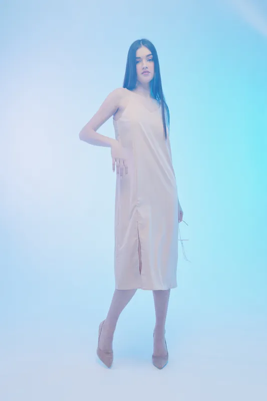 Young woman in a beige dress poses confidently in a soft blue studio light. Her long hair is straight and she wears high heels. Concept of woman beauty fashion elegance.