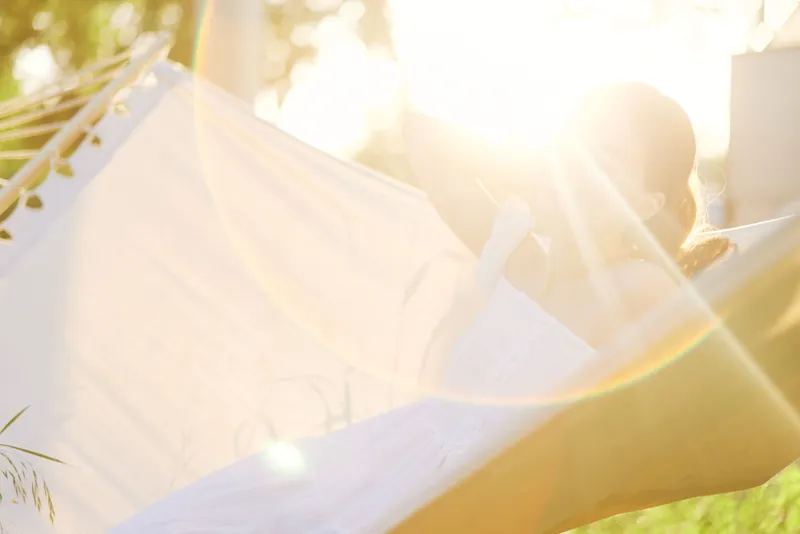 A serene woman relaxing in a hammock surrounded by nature, illuminated by soft sunlight, showcasing a peaceful expression in a tranquil outdoor setting