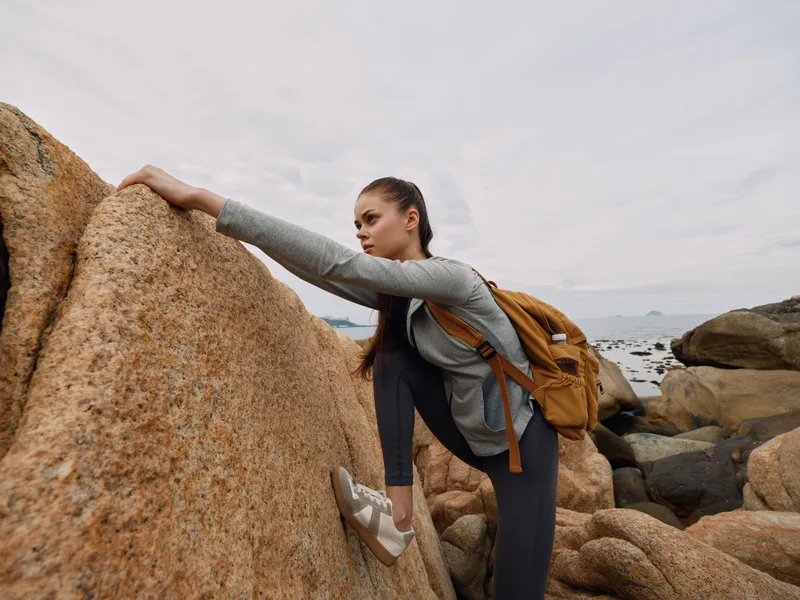 Young woman climbing rocks in athletic wear, showcasing determination and adventure in a coastal landscape, perfect for outdoor and fitness concepts
