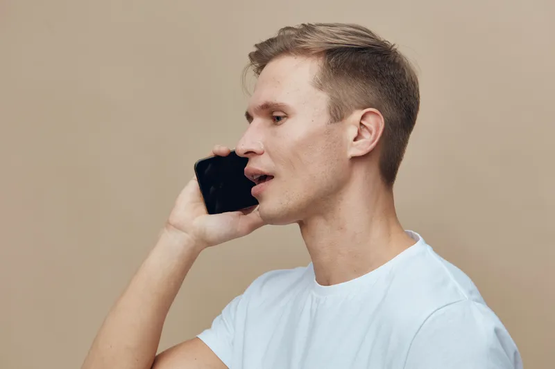 young caucasian man talking on smartphone side view wearing white t-shirt isolated on beige background digital nomad concept communication technology