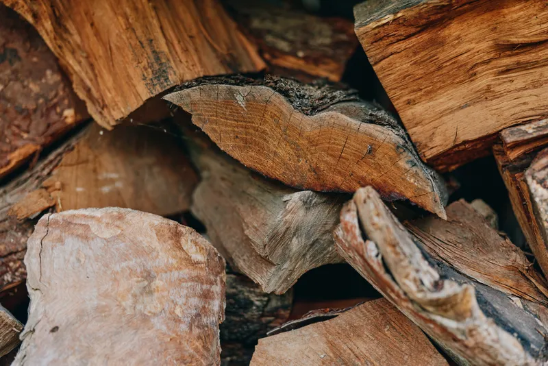 firewood, stacked logs, woodpile, chopped wood, hardwood, bark, timber, log texture closeup of split fireplace fuel in a rustic backyard pile, dry sawn timber for cabin heating, warm brown tones.