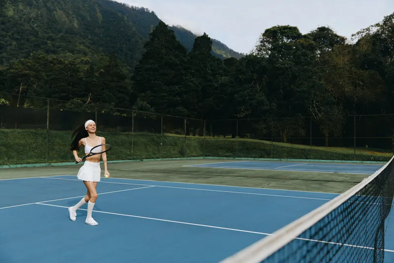Joyful young woman playing tennis on a beautiful outdoor court surrounded by lush greenery, showcasing athleticism and sporty style in a lively setting