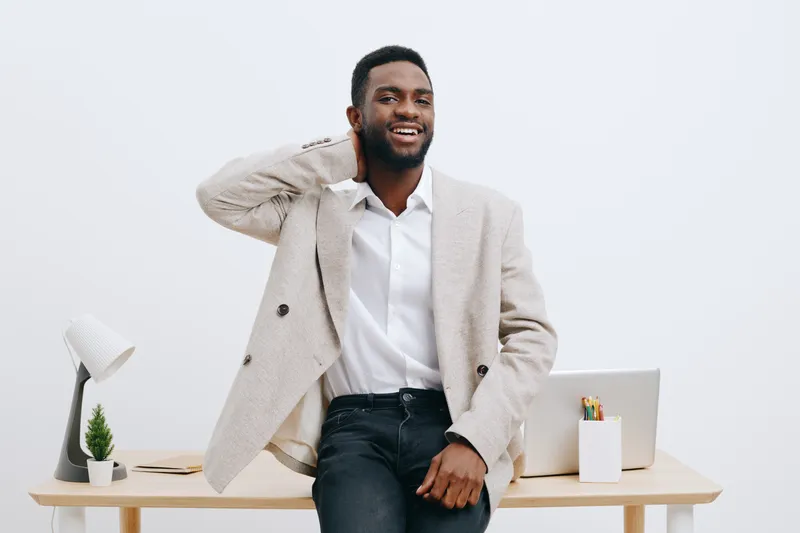 Smiling man in smart casual attire standing in modern workspace, cheerful expression, relaxed pose, white background, professional environment, casual outfit, young adult male. People lifestyle concep