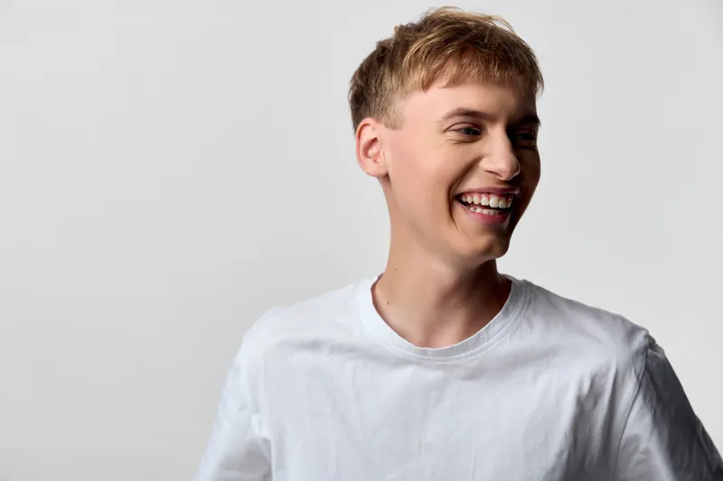 Smiling man in a white shirt exudes casual happiness, a bright expression captured in a clean studio setting. Cheerful mood, relaxed demeanor, and approachable style emphasize positive energy for