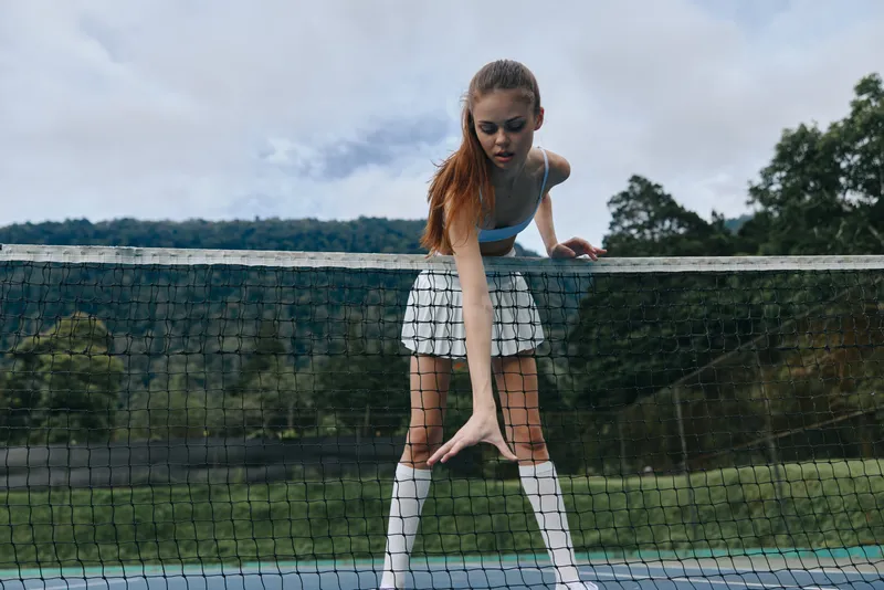 Young female tennis player preparing to hit the ball, wearing a sporty outfit, demonstrating focus and determination on the tennis court surrounded by nature