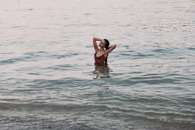 Woman relaxing in calm sea water during sunset, enjoying peaceful moment with soft colors and serene waves around her body.