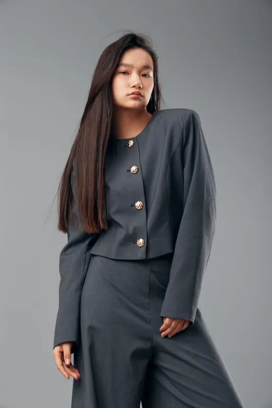 Young woman standing in modern gray suit with long straight hair posing in studio with light gray background. Fashion, confidence, portrait, serious expression and stylish clothing for business or