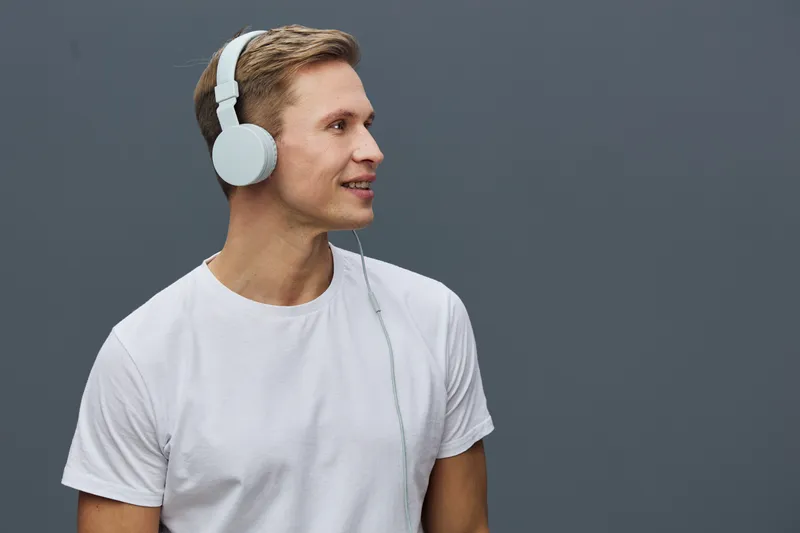 smiling young caucasian man wearing white headphones look side casual t-shirt isolated gray background digital detox technology concept