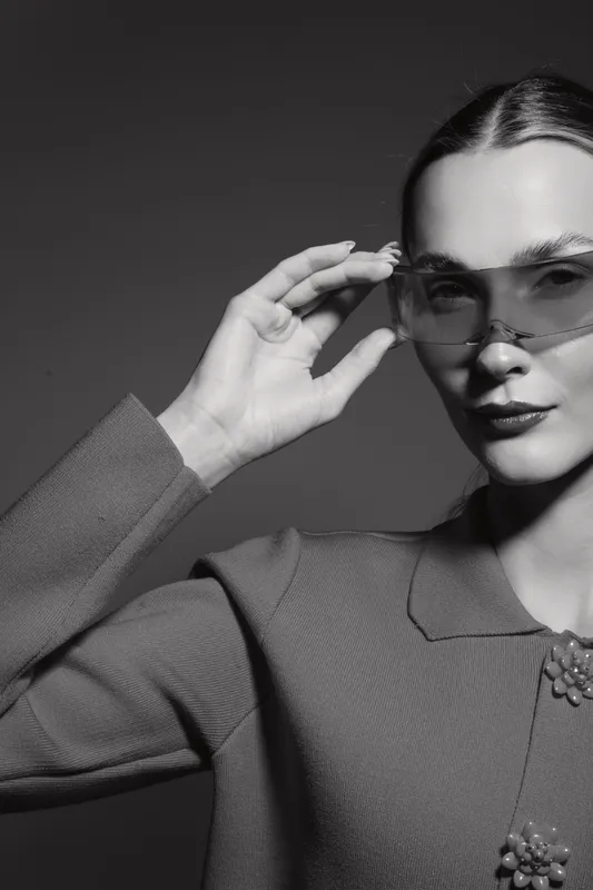Portrait of a white woman with pale skin adjusting transparent sunglasses, dressed in textured fabric with decorative buttons. Concept of fashion and elegance.
