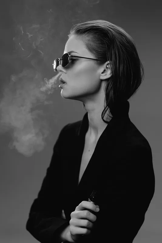 Stylish woman vaping in black and white portrait with sunglasses and smoke around her.