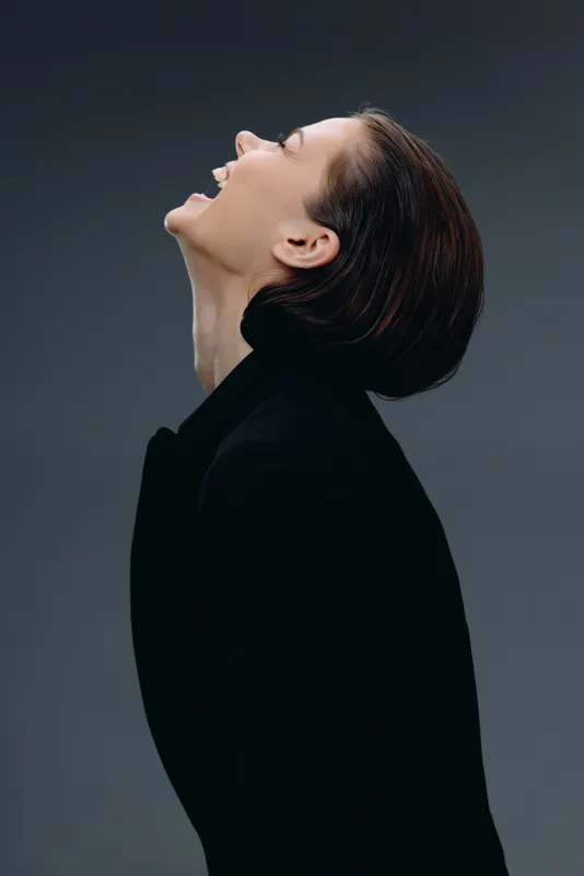 Smiling woman with short hair dressed in black jacket enjoying a joyful moment against dark background