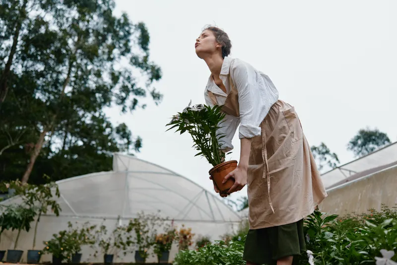 Woman in an apron caring for plants, showcasing seasonal gardening emotions and sustainable practices in a lush green background