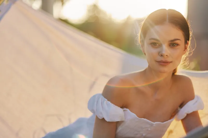 Young model in a white dress enjoying a sunny day outdoors, exuding confidence and warmth, with a blurred nature background, perfect for summer and joyful themes
