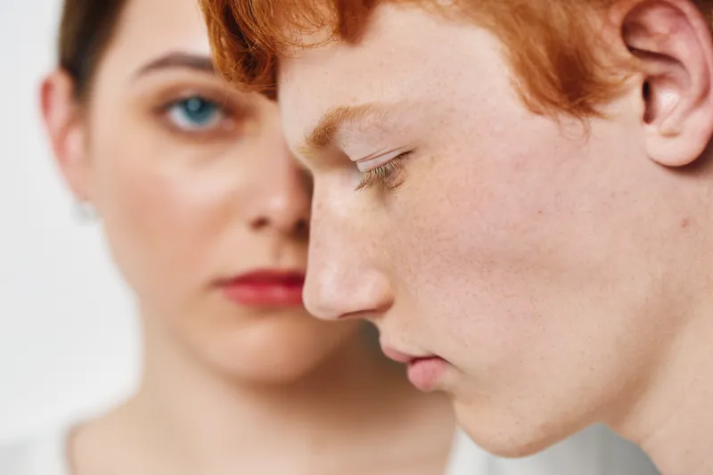 Young redhead man and woman with sensitive expression closeup, emotional calm mood, pale skin and blue eyes with natural light on white background.