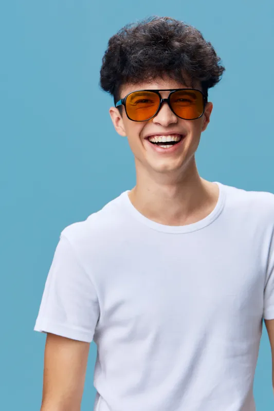 smiling man wearing orange sunglasses in casual white t-shirt, curly hair and cheerful expression on blue background, youthful and fresh vibe