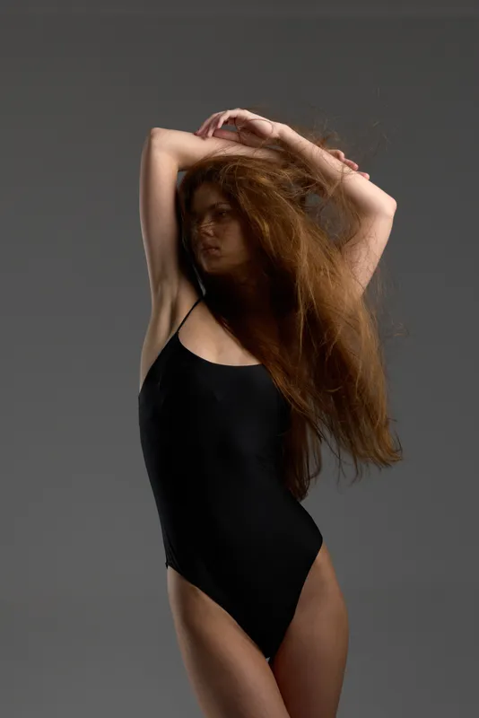 Woman posing in black swimsuit with long red hair and soft lighting, fashion concept, studio background