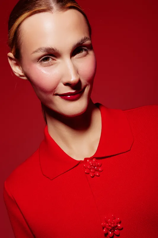 Portrait of a smiling woman with red lipstick and blush wearing a red collared shirt against a red background. Concept of fashion, beauty, and confident expression.