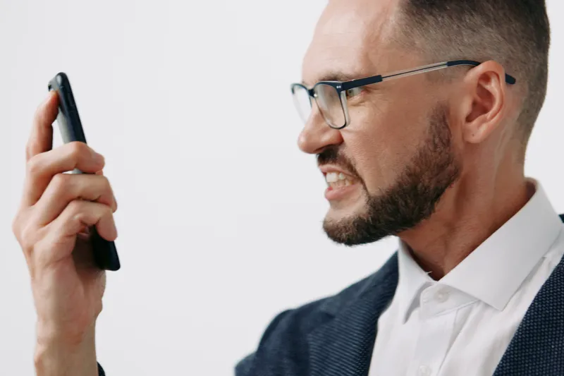 A focused business professional man in glasses holds a phone, expressing determination against a bold isolated colored background, conveying ambition, urgency, and clear communication in a dynamic